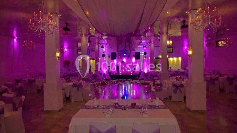 Salle de réception décorée avec des tables dressées, éclairage violet et une scène au fond avec des projecteurs.