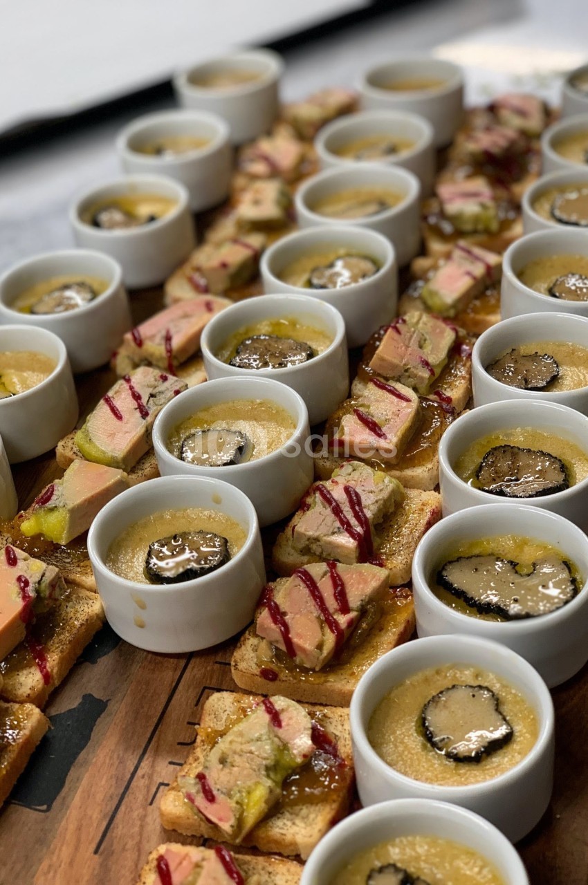 Assortiment de verrines et toasts garnis de foie gras, truffes et sauces, disposés sur une planche en bois.