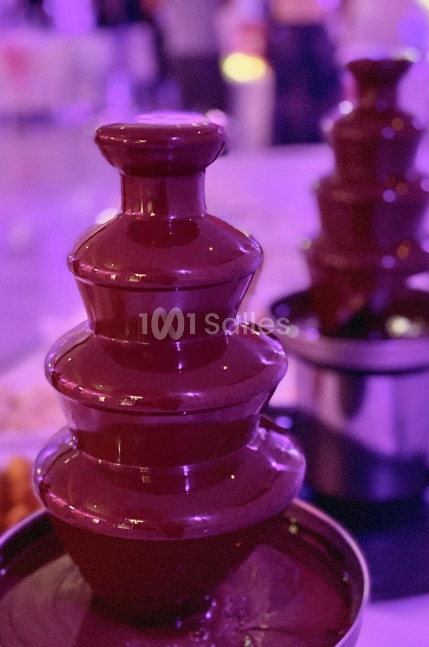Fontaine à chocolat en fonctionnement avec plusieurs étages, entourée d'une ambiance lumineuse violette.