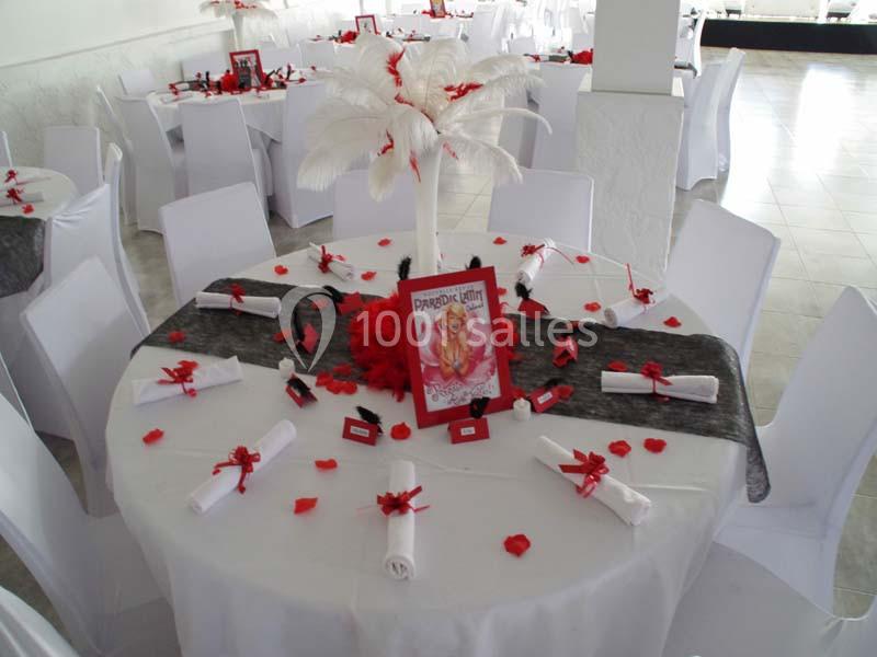 Table décorée avec des plumes blanches, pétales rouges, serviettes roulées et un cadre central dans une salle de réception.