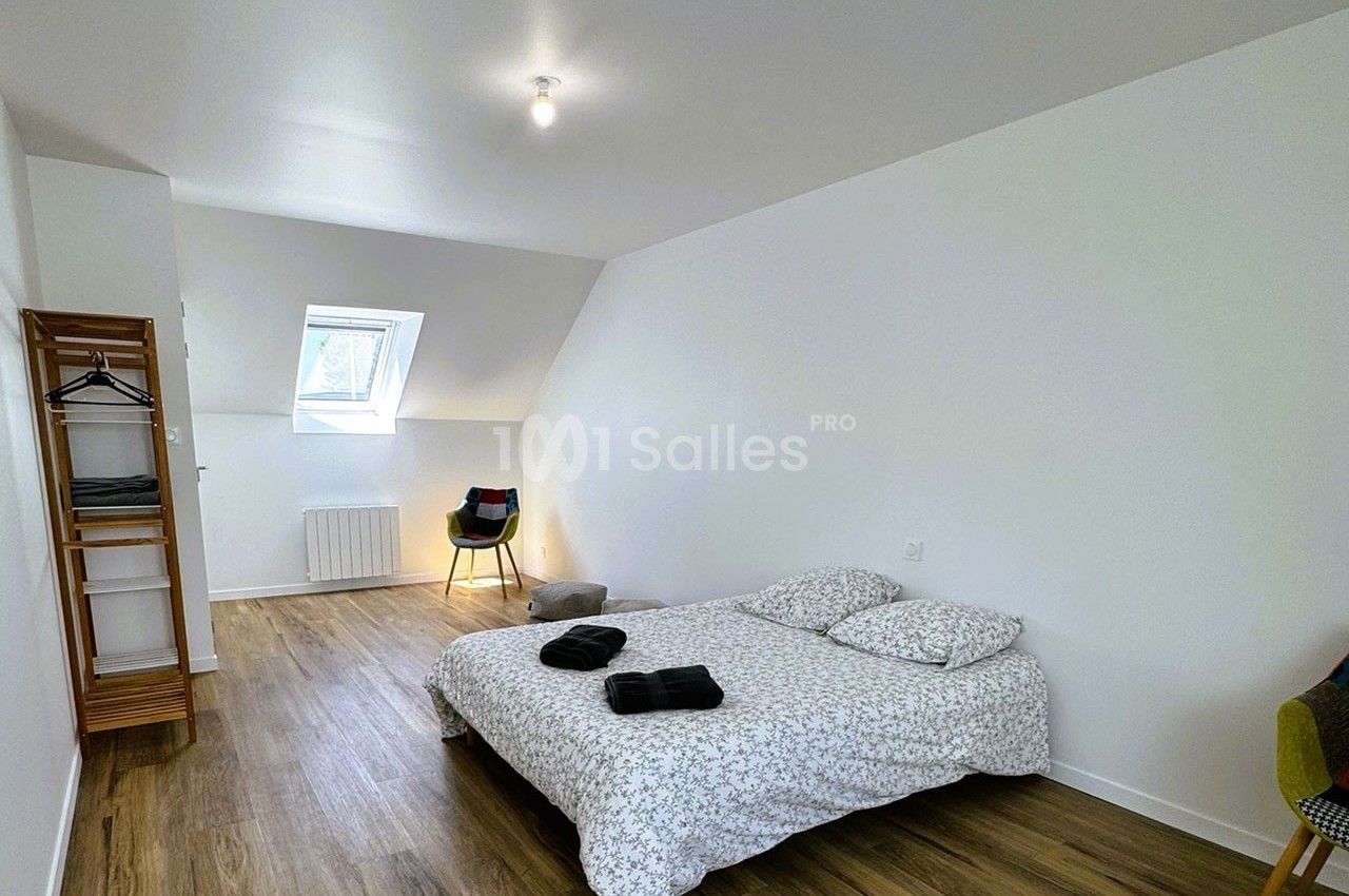 Chambre lumineuse avec lit double, parquet, portant en bois, chaise et fenêtre de toit.