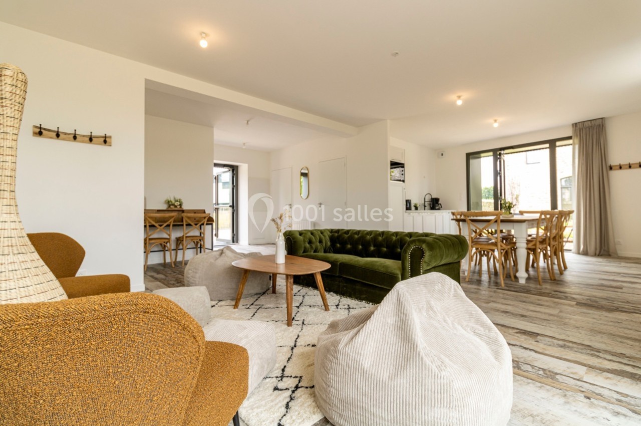 Salon spacieux avec canapé vert, fauteuils, poufs, table basse, parquet clair et grande luminosité naturelle.