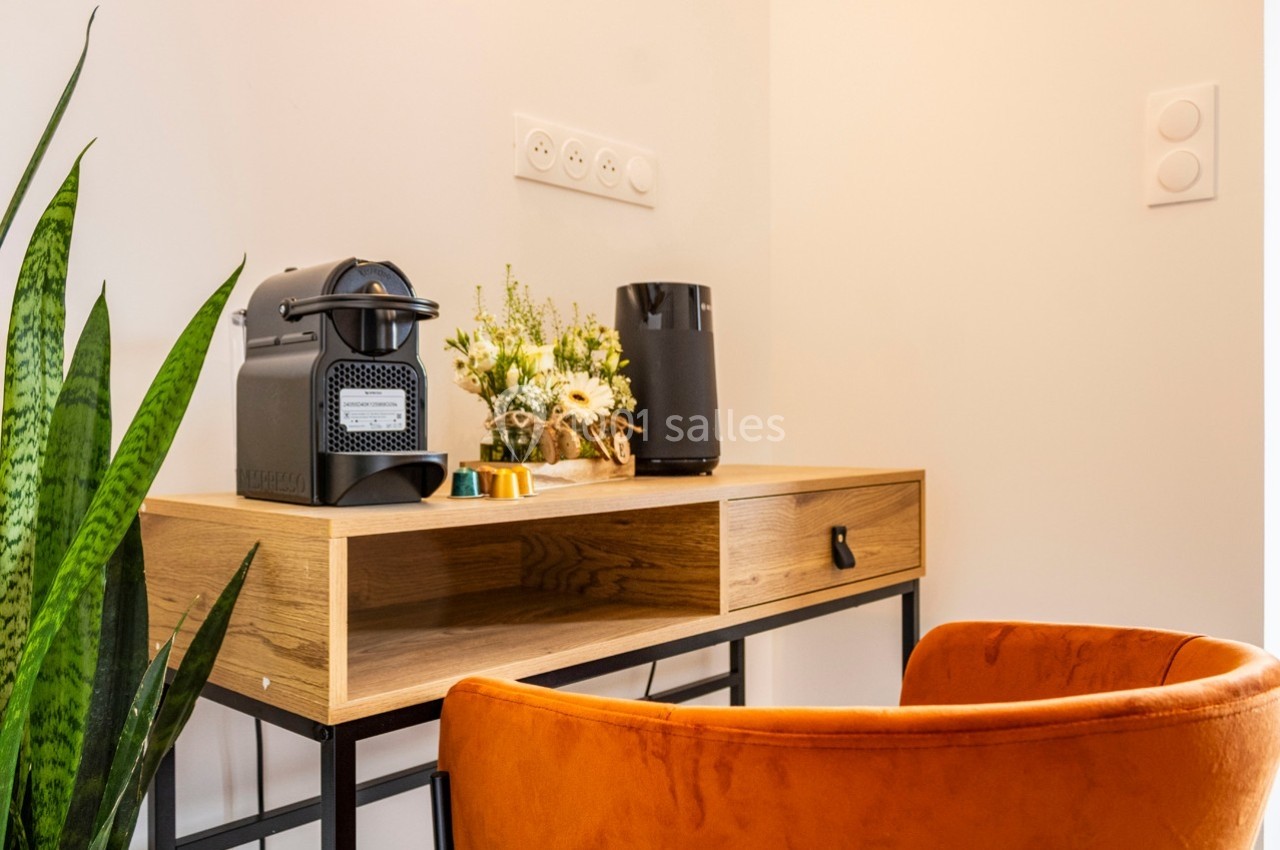 Coin bureau avec une chaise orange, une machine à café, des fleurs et une plante verte sur un bureau en bois.