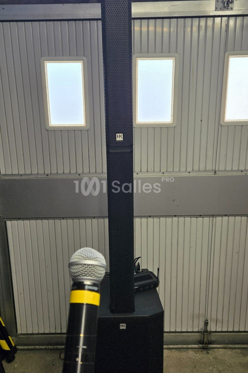 Système de sonorisation avec une colonne d'enceintes et un microphone tenu devant, installé dans un garage.