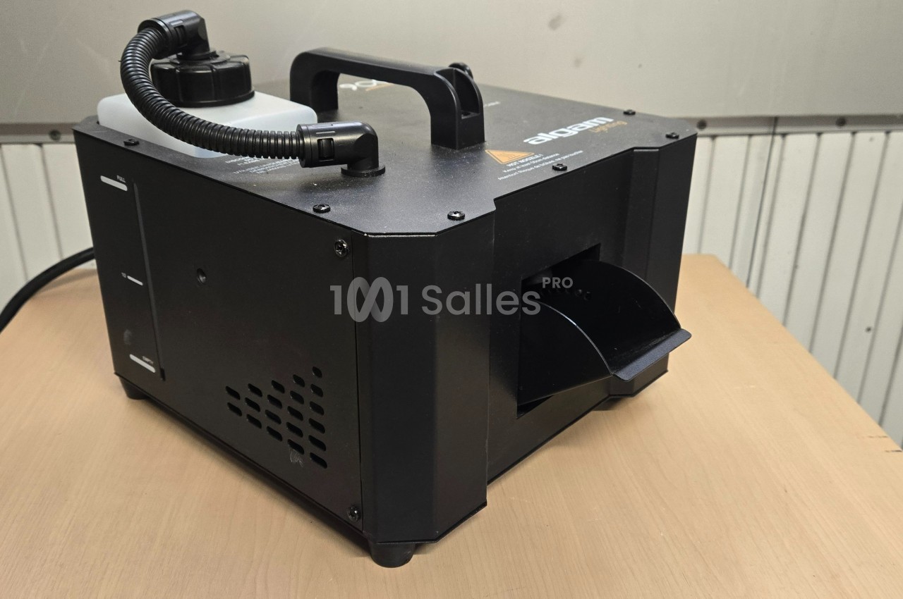 Machine à fumée noire posée sur une table en bois, avec un réservoir et une poignée sur le dessus.