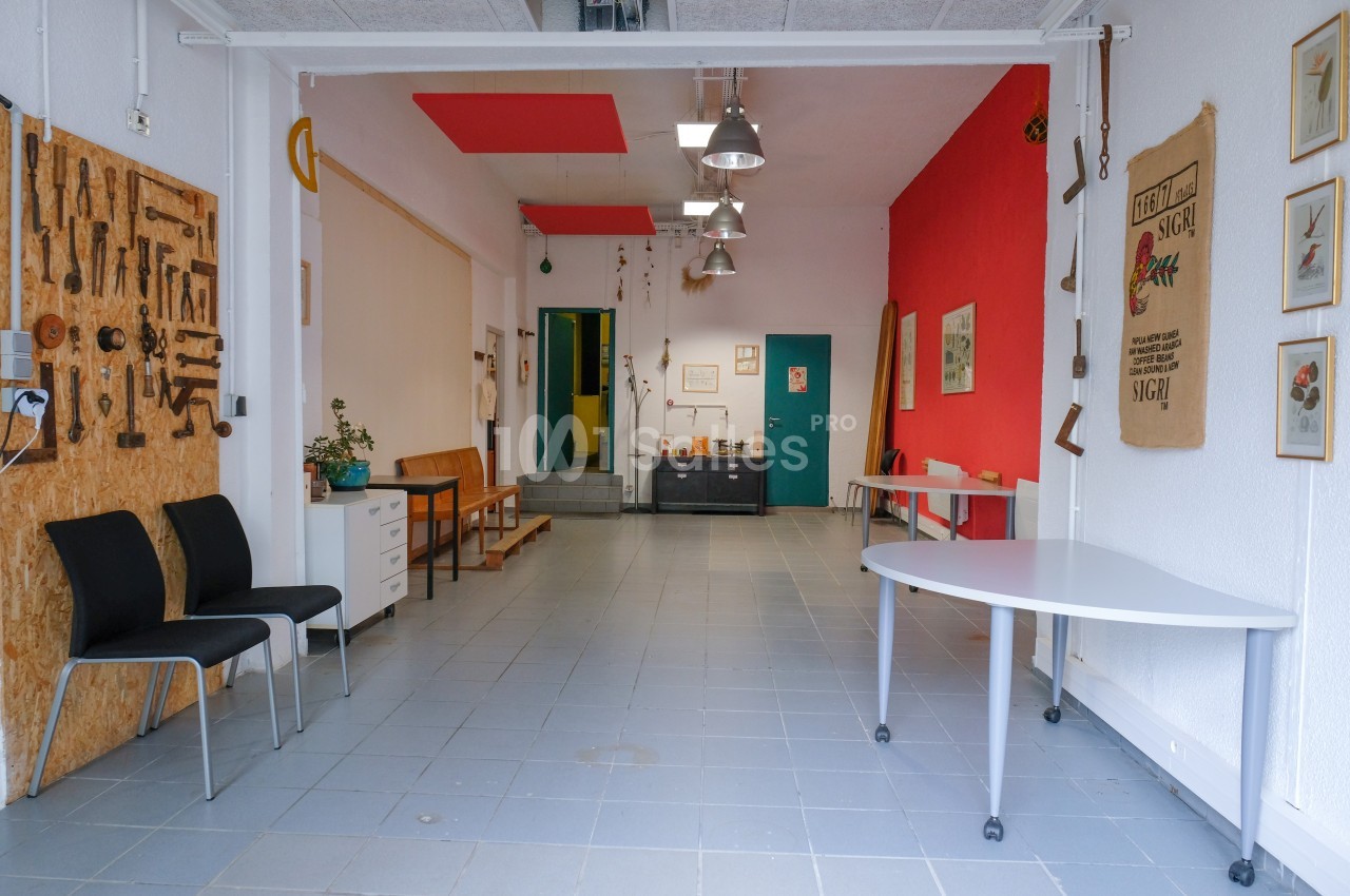 Atelier lumineux avec outils accrochés au mur, mobilier simple et espace dégagé sur un sol en carrelage gris.