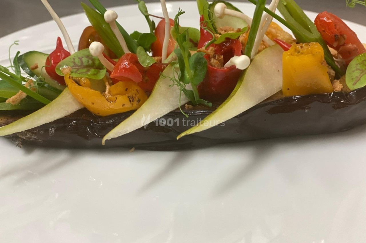 Aubergine grillée garnie de légumes colorés, tranches de poire et pousses fraîches, présentée sur une assiette blanche.