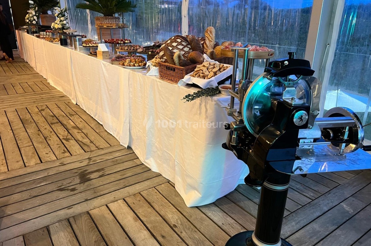 Buffet de pains et viennoiseries disposé sur une longue table blanche, avec une trancheuse en premier plan.