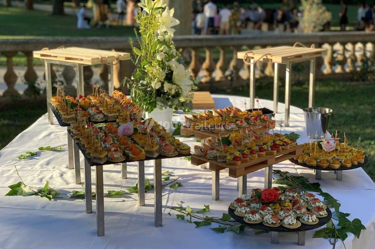 Buffet en plein air avec des amuse-bouches variés disposés sur des présentoirs, entourés de décorations florales.
