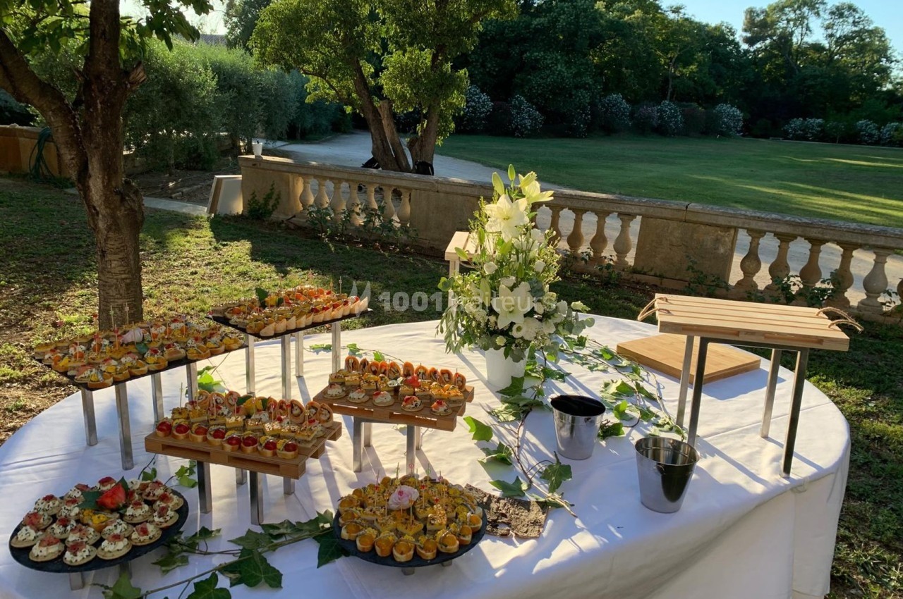 Buffet en plein air avec des amuse-bouches variés disposés sur des présentoirs, entouré de verdure et d'une décoration…