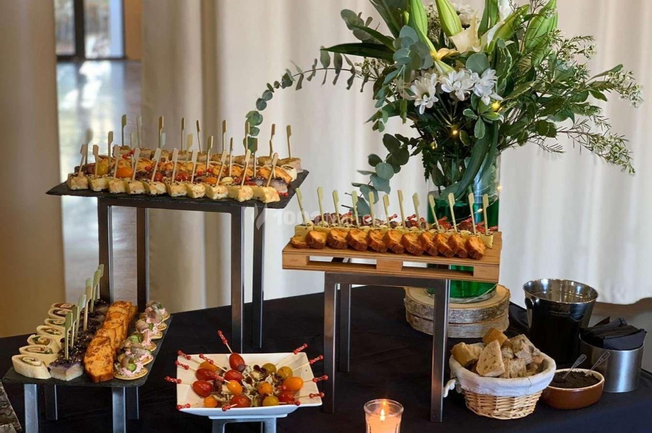 Buffet avec des amuse-bouches variés présentés sur des supports, accompagné d'une composition florale et d'une bougie.