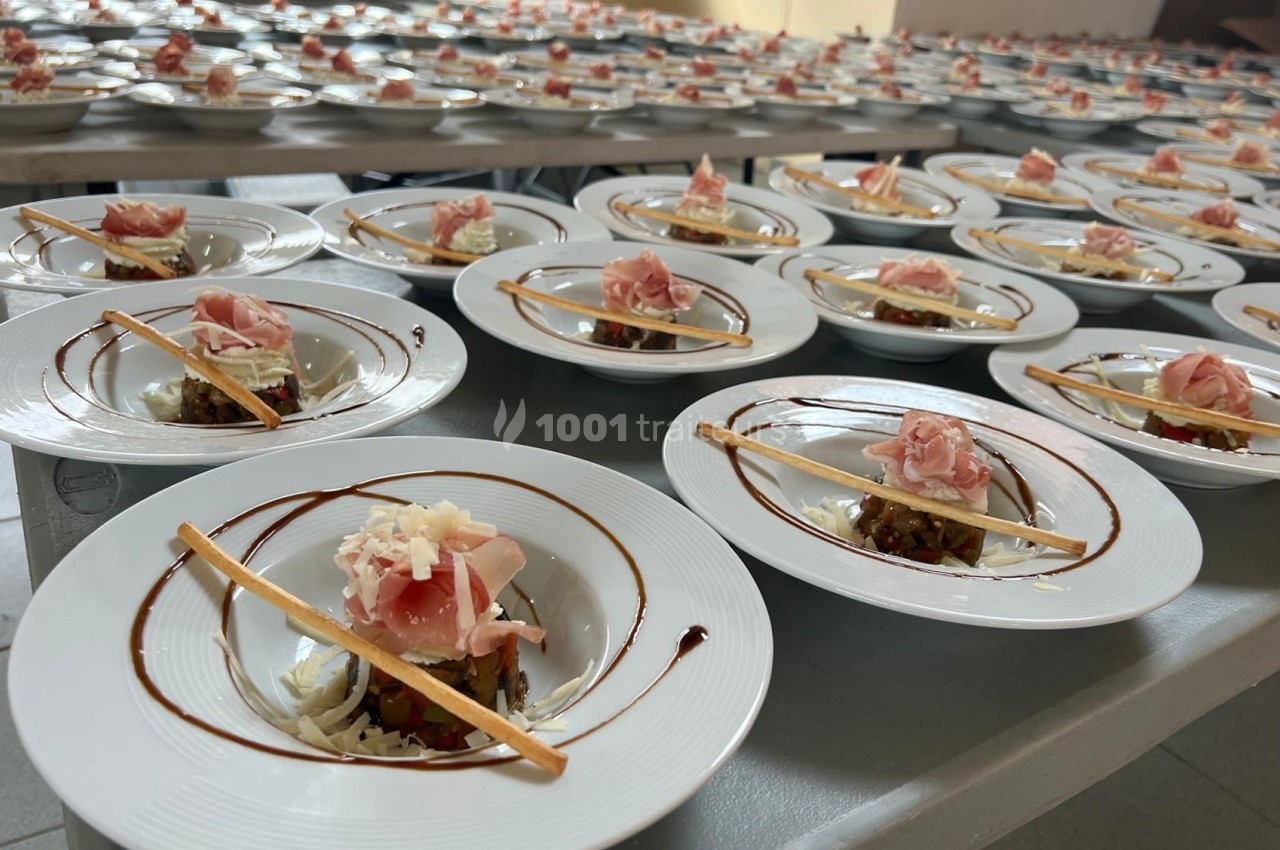 Assiettes dressées avec tartare de légumes, jambon cru, copeaux de fromage et filet de balsamique sur tables alignées.