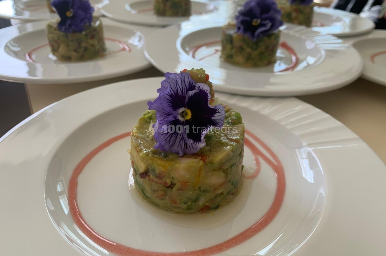 Tartare de légumes colorés garni d'une fleur comestible violette, présenté sur une assiette blanche décorée.