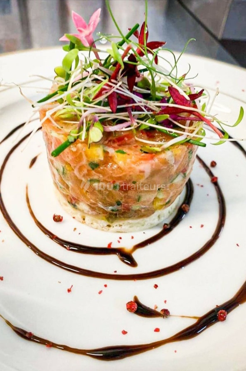 Tartare de saumon garni de jeunes pousses et entouré de filet de sauce balsamique sur une assiette blanche.