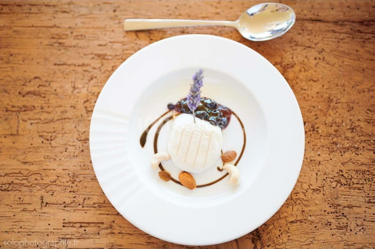 Assiette de fromage frais décorée de sauce balsamique, fruits secs, confiture et une fleur de lavande.