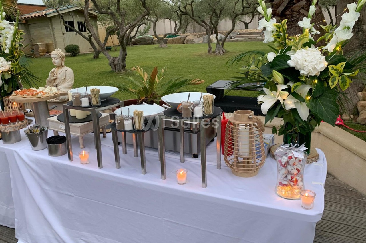 Buffet en plein air avec plats variés, décoré de fleurs blanches, bougies et une statue de Bouddha.