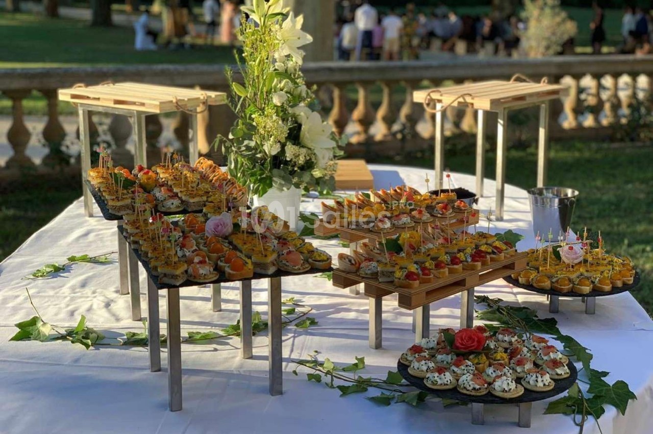 Table dressée en extérieur avec des plateaux de canapés variés, décorée de fleurs et de feuillage.