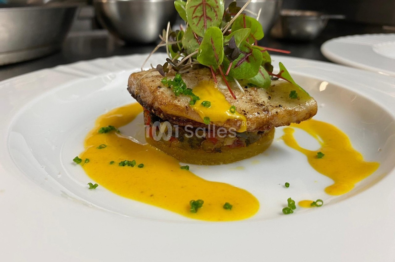 Plat gastronomique composé de poisson grillé, légumes, sauce jaune et jeunes pousses, présenté sur une assiette blanche.