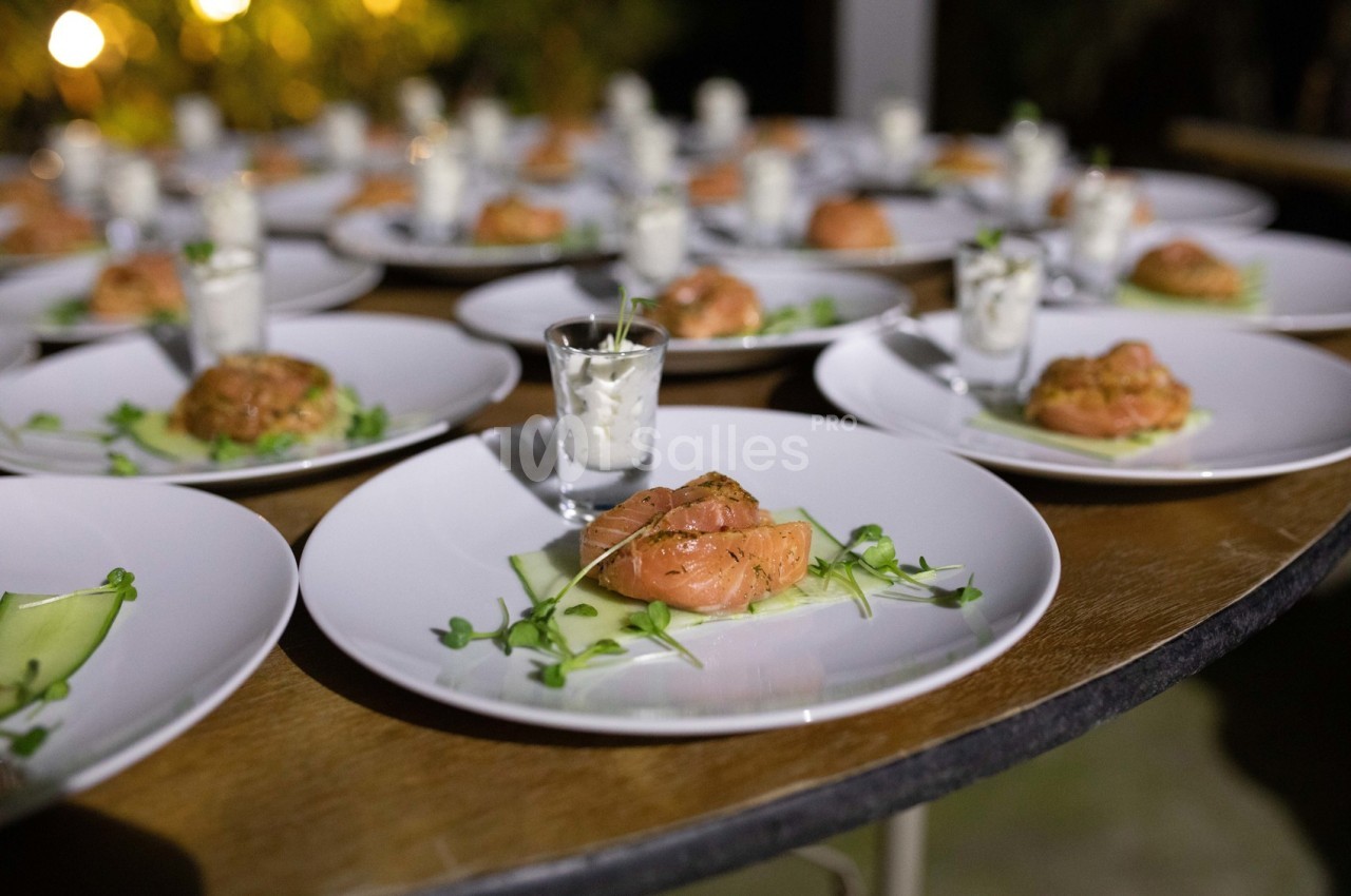Assiettes dressées avec du saumon fumé, des pousses vertes et des verrines de sauce, disposées sur une grande table.