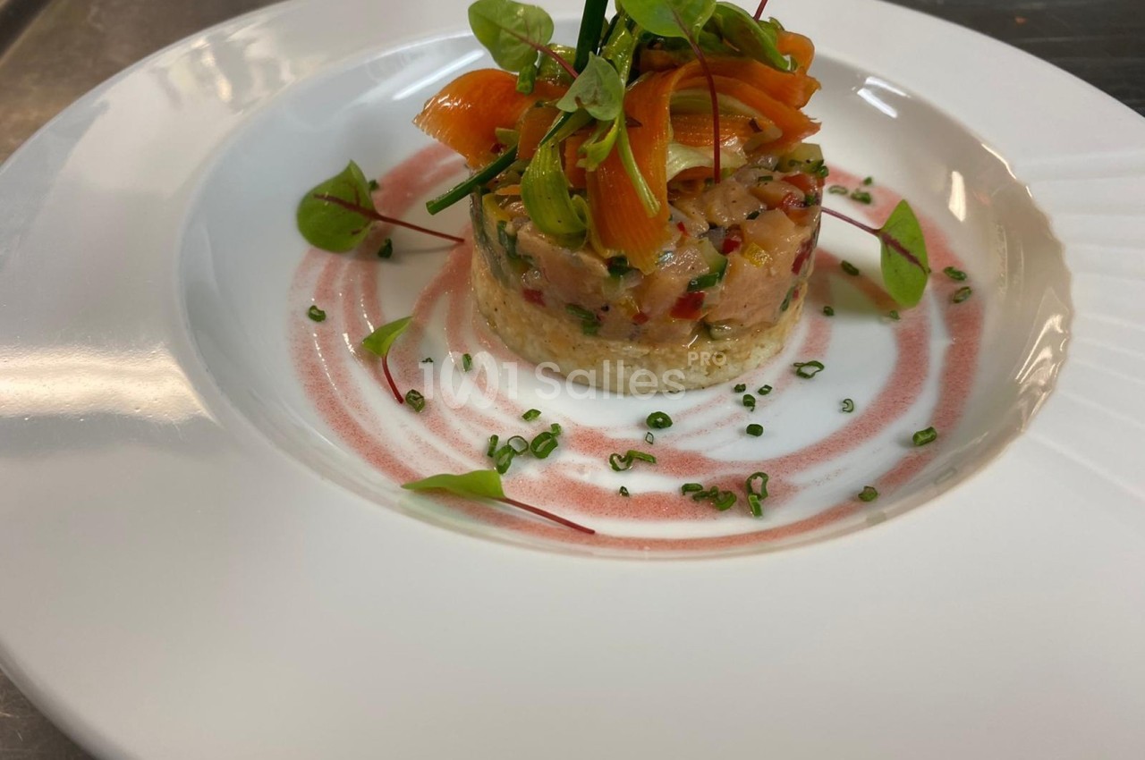 Tartare de saumon dressé en cercle, garni de fines herbes et accompagné d'une sauce décorative dans une assiette blanche.