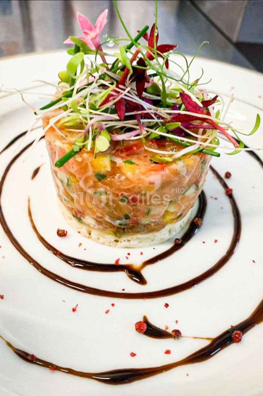 Tartare de saumon dressé avec des pousses et des herbes fraîches, entouré de traits de sauce balsamique.