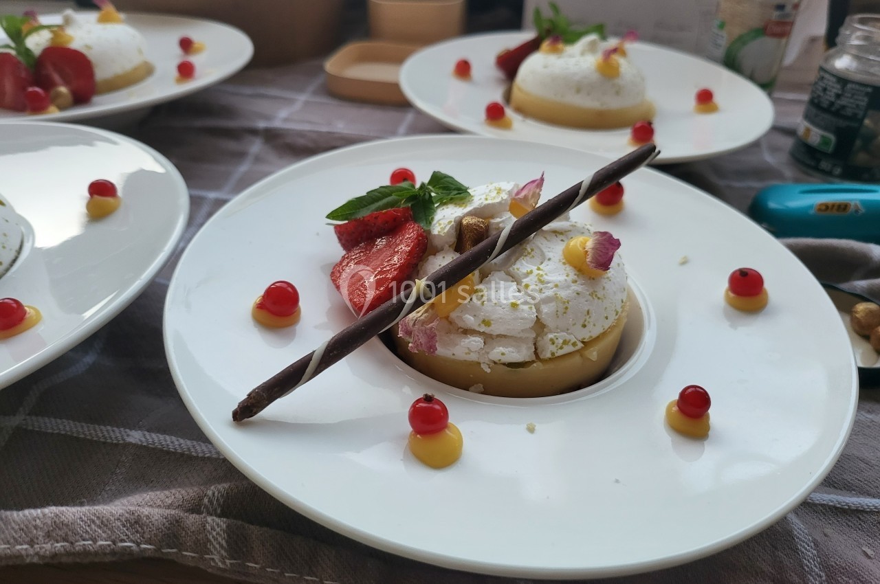 Assiette de dessert décorée avec mousse blanche, fraises, perles rouges, feuille de menthe et bâtonnet chocolaté.