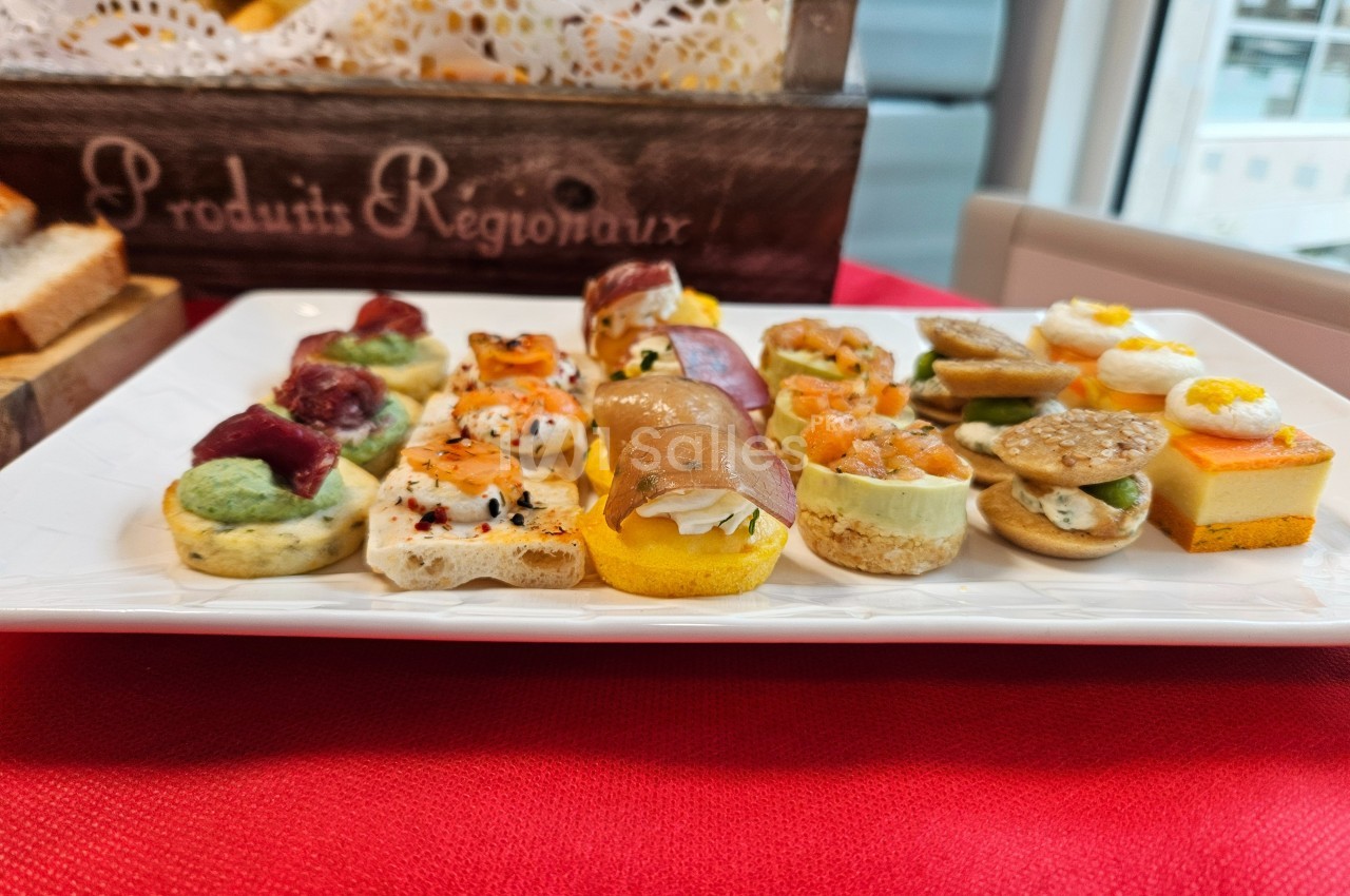 Assortiment de canapés variés présentés sur une assiette blanche, posé sur une nappe rouge.
