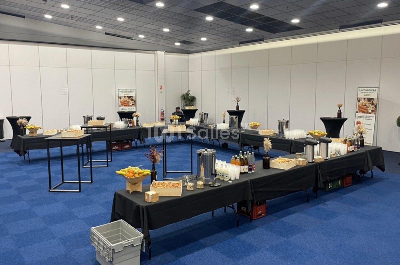 Buffet de petit-déjeuner avec boissons chaudes, jus, viennoiseries et fruits, disposé sur des tables dans une salle.
