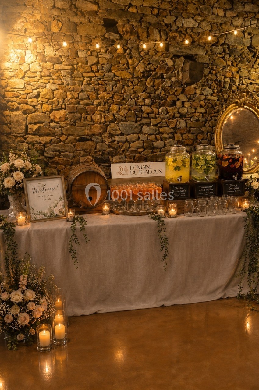 Table décorée pour un événement avec fleurs, bougies, boissons en distributeurs et mur en pierre en arrière-plan.