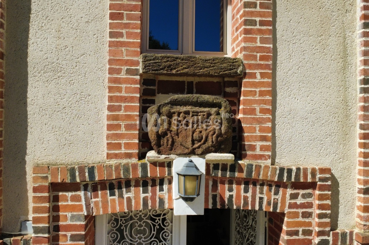Détail d'une façade en briques avec une sculpture en pierre au-dessus d'une fenêtre et une applique murale.
