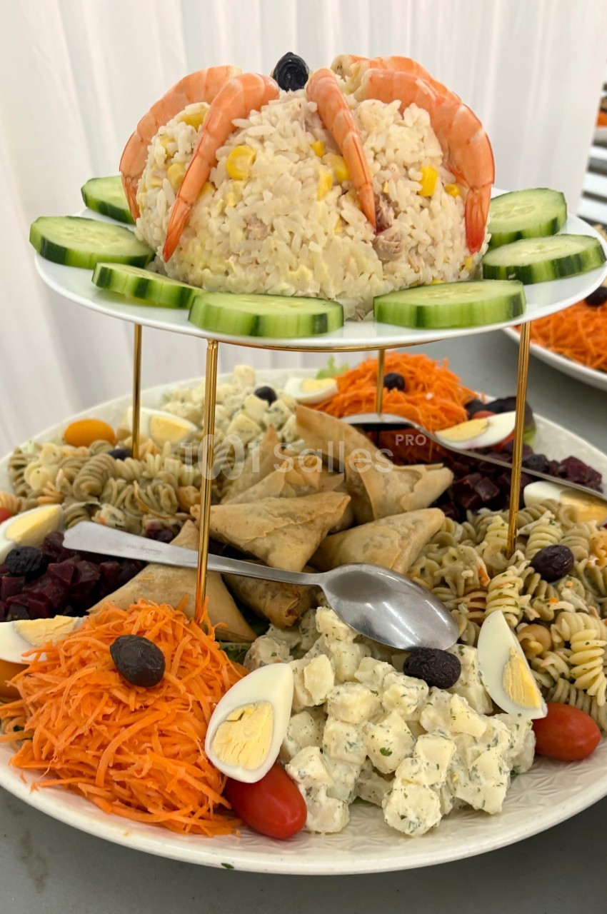 Assiette garnie de riz aux crevettes, crudités, salades variées, samoussas et œufs durs, présentée sur un support à étages.