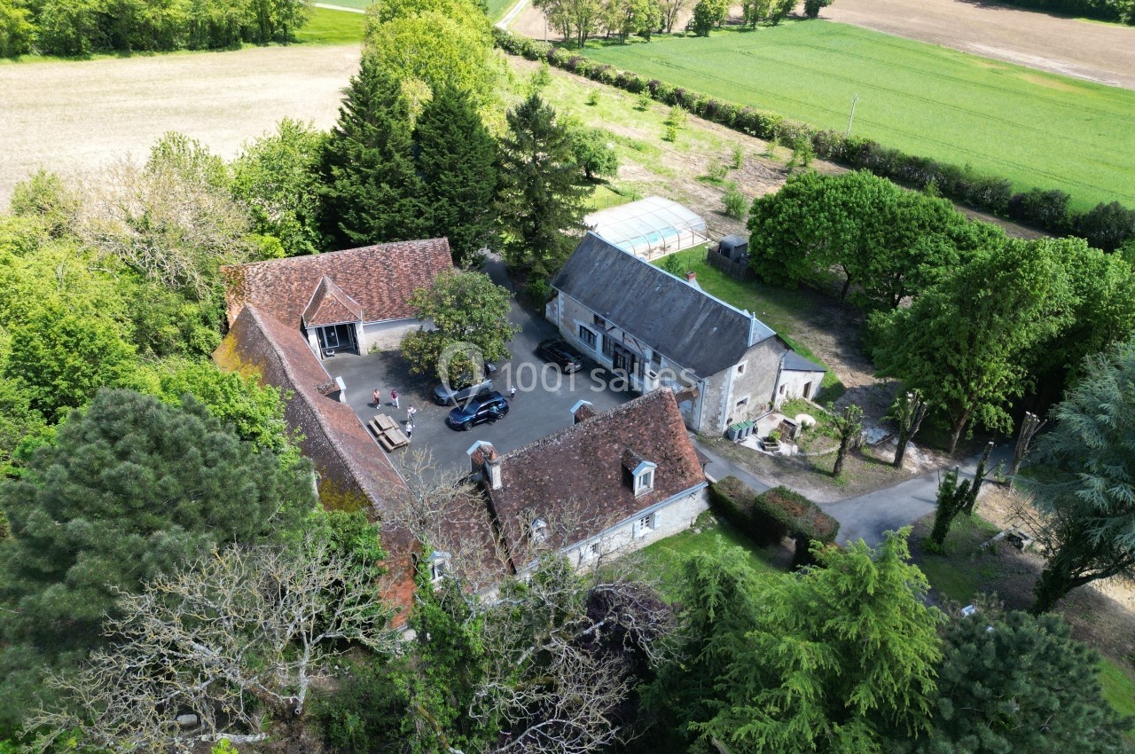 Vue aérienne d'un domaine rural avec bâtiments en pierre, toits en tuiles, arbres et champs environnants.