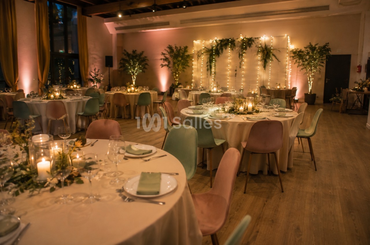 Salle de réception décorée avec des tables rondes, des chaises colorées et des guirlandes lumineuses sur des plantes.