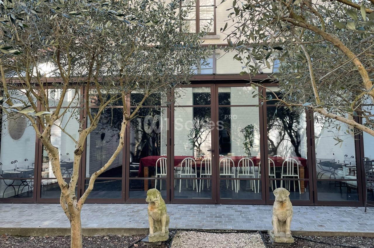 Façade vitrée d'un bâtiment donnant sur une terrasse avec des arbres et deux statues de chiens en pierre.
