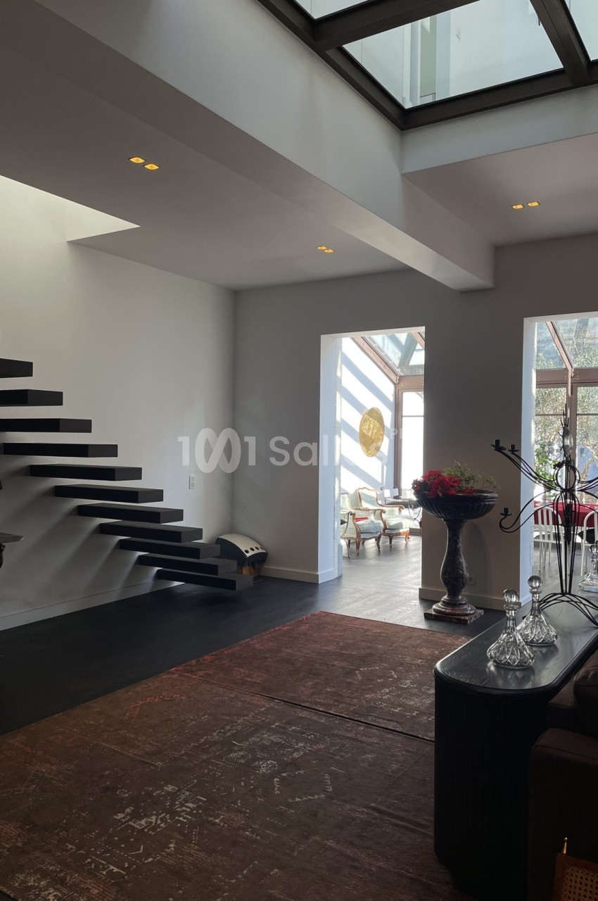 Intérieur moderne avec escalier flottant noir, grande baie vitrée et mobilier élégant dans un espace lumineux.