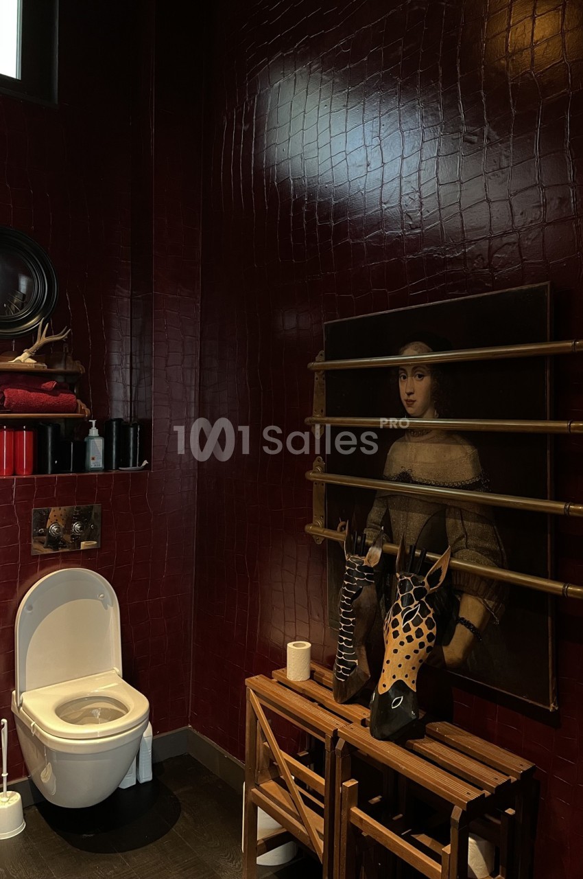 Salle de bain avec murs rouge foncé, toilette blanche, étagères en bois et tableau décoratif.