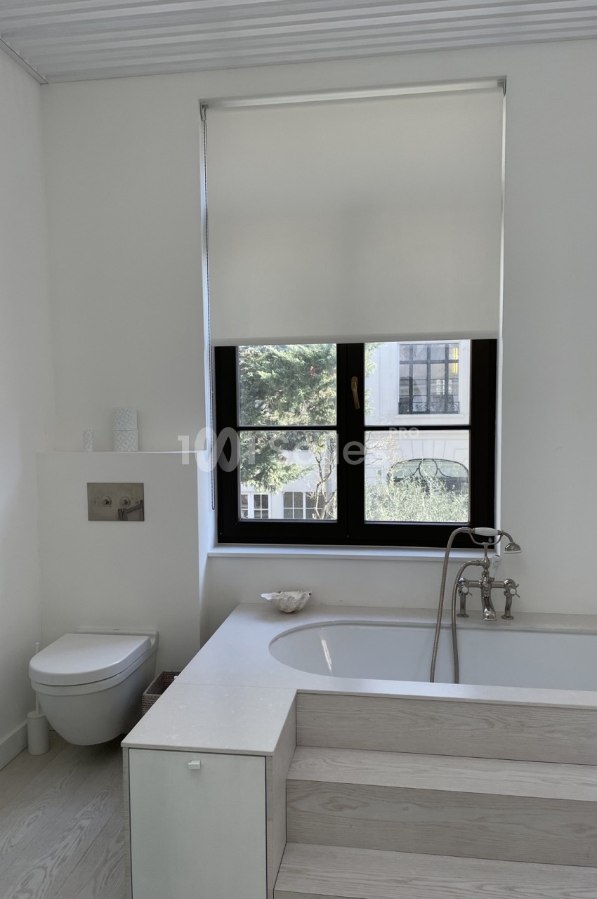 Salle de bain lumineuse avec baignoire, toilettes suspendues et fenêtre donnant sur un jardin.