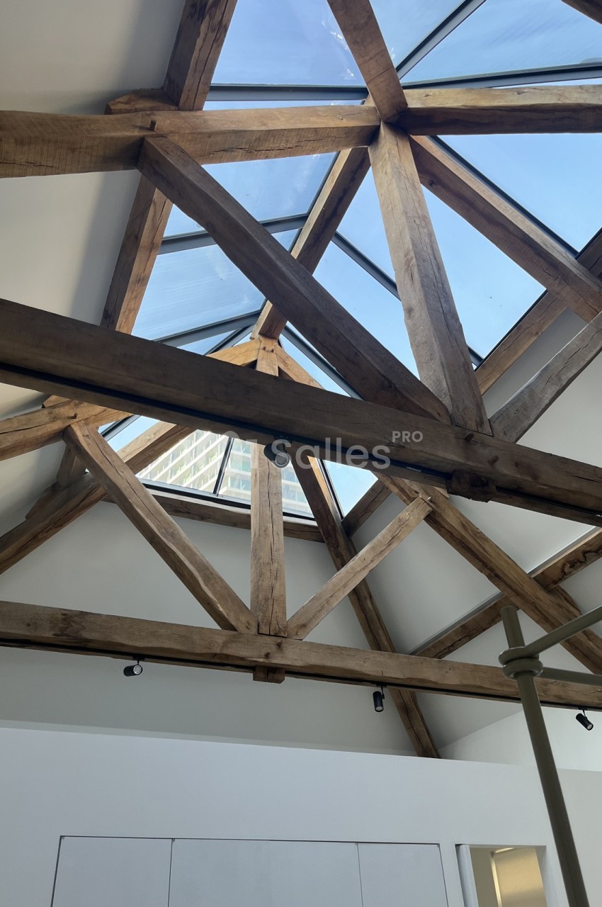 Charpente en bois apparente sous un plafond incliné avec une grande verrière laissant entrer la lumière naturelle.