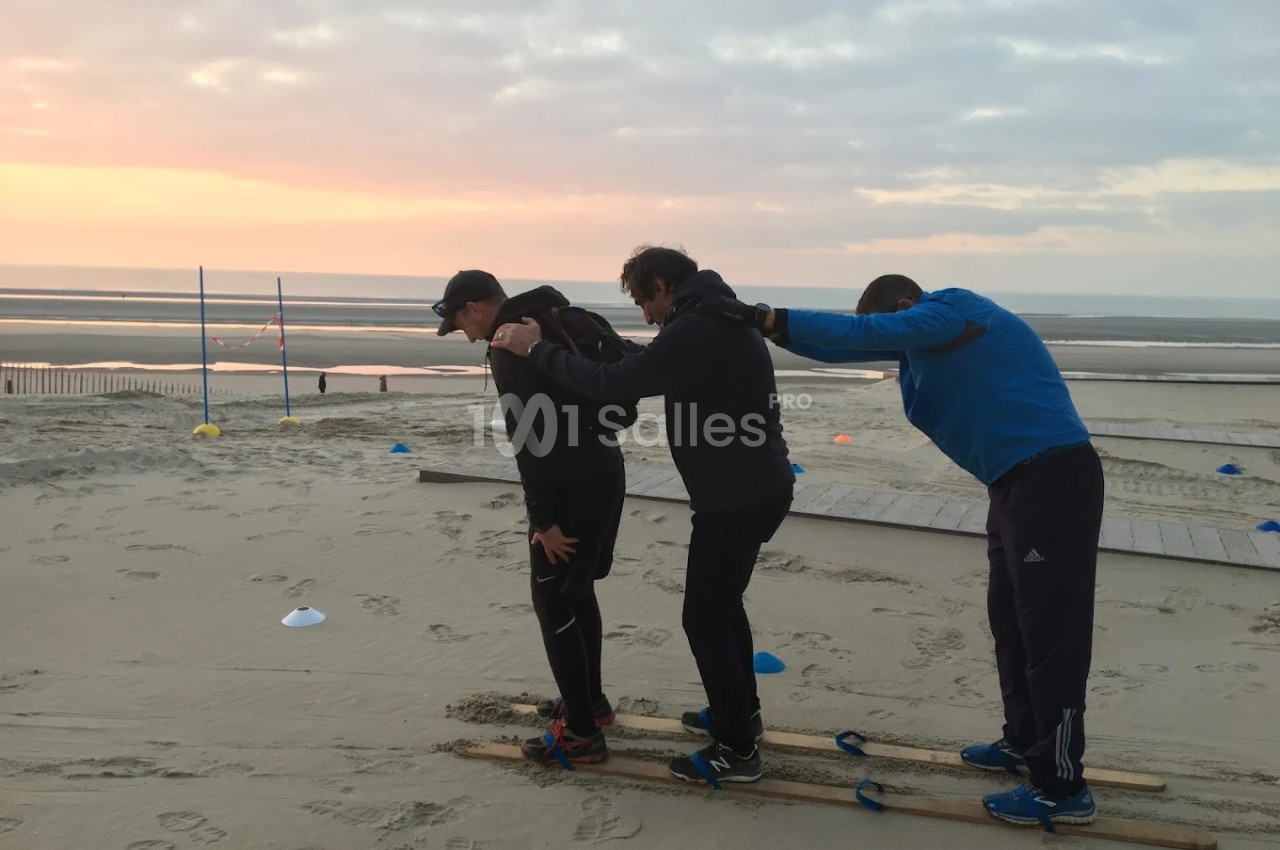 Trois personnes coopèrent sur des skis en bois sur une plage au lever du soleil.
