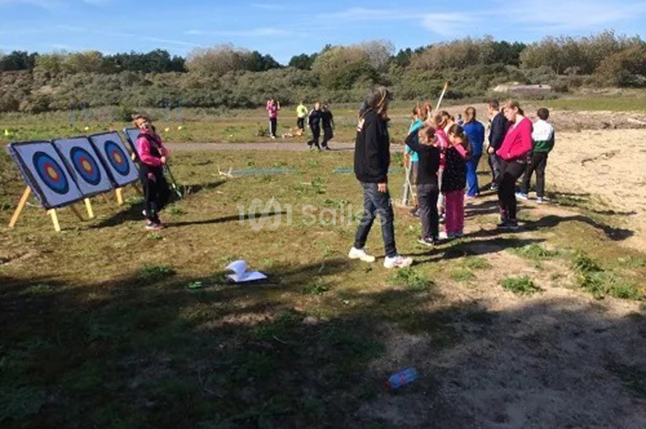 Un groupe de personnes apprend le tir à l'arc en plein air, face à des cibles installées sur un terrain dégagé.