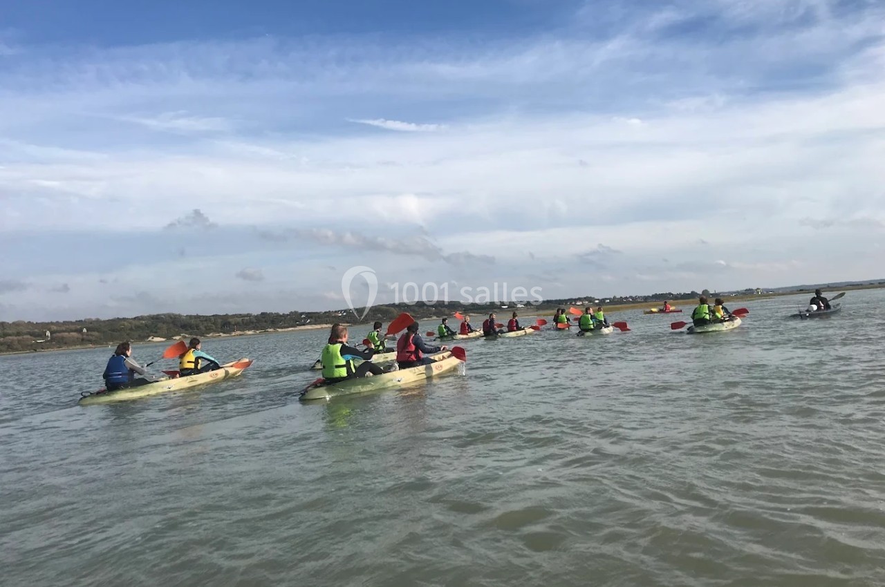 Groupe de personnes pagayant en kayak sur une étendue d'eau sous un ciel partiellement nuageux.
