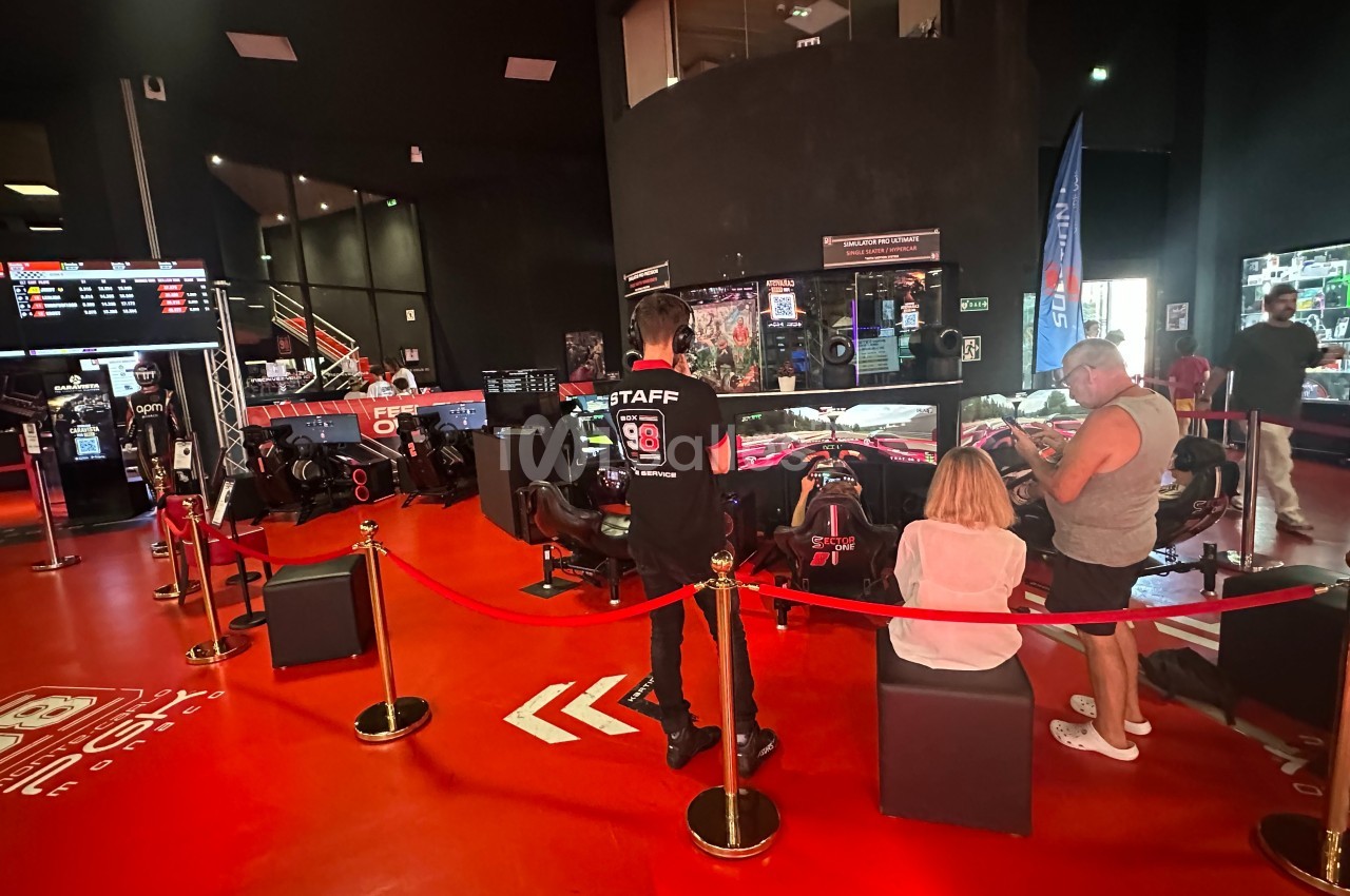 Des visiteurs observent des simulateurs de course automobile dans un espace intérieur avec un sol rouge et des écrans.