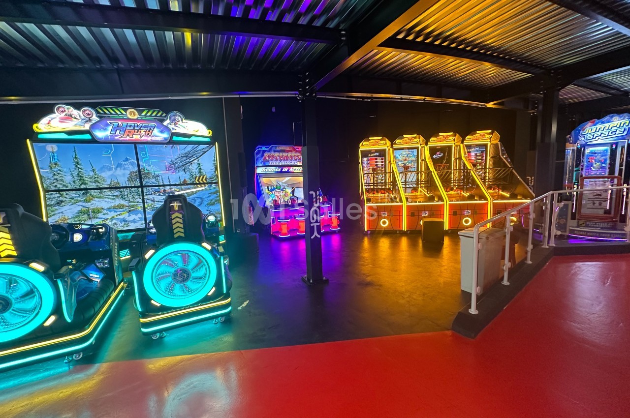 Salle d'arcade avec des bornes de jeux lumineuses et colorées alignées sous un éclairage tamisé.