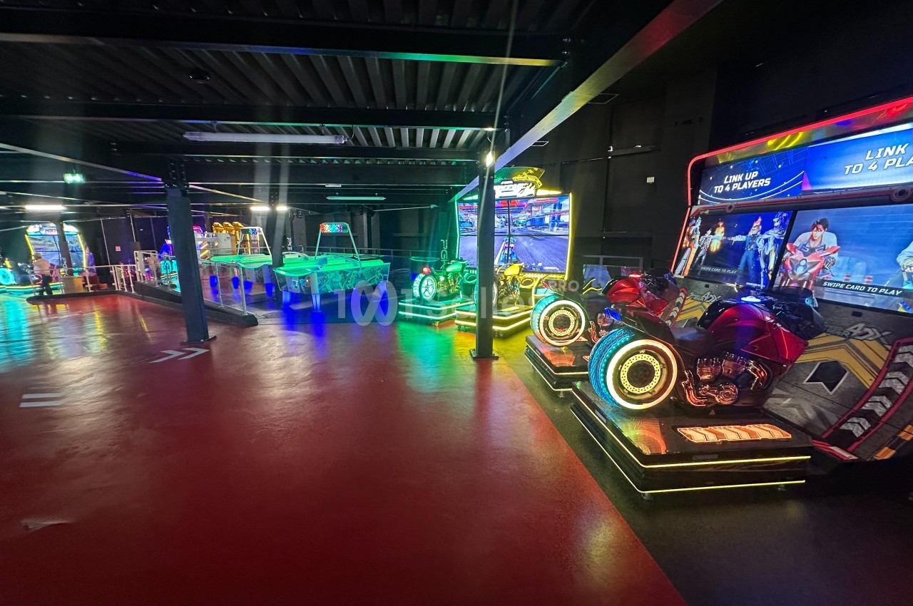 Salle d'arcade avec jeux interactifs lumineux, dont des simulateurs de moto et une table de hockey sur air.
