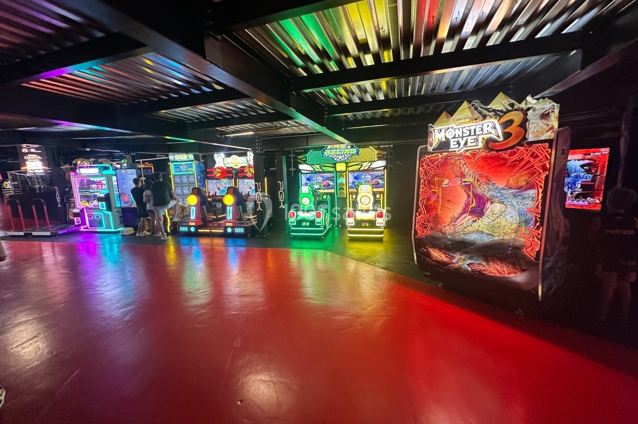 Salle d'arcade avec plusieurs bornes de jeux lumineuses, dont une intitulée ’Monster Eye 3’, sur un sol rouge.