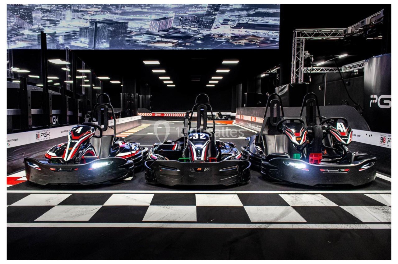 Trois karts alignés sur une piste intérieure éclairée, prêts pour une course, avec un décor urbain en arrière-plan.