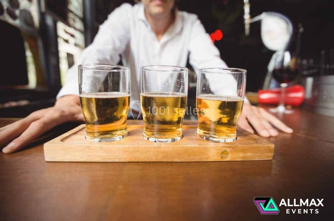 Trois verres de bière blonde alignés sur un plateau en bois, posés sur une table dans un bar.