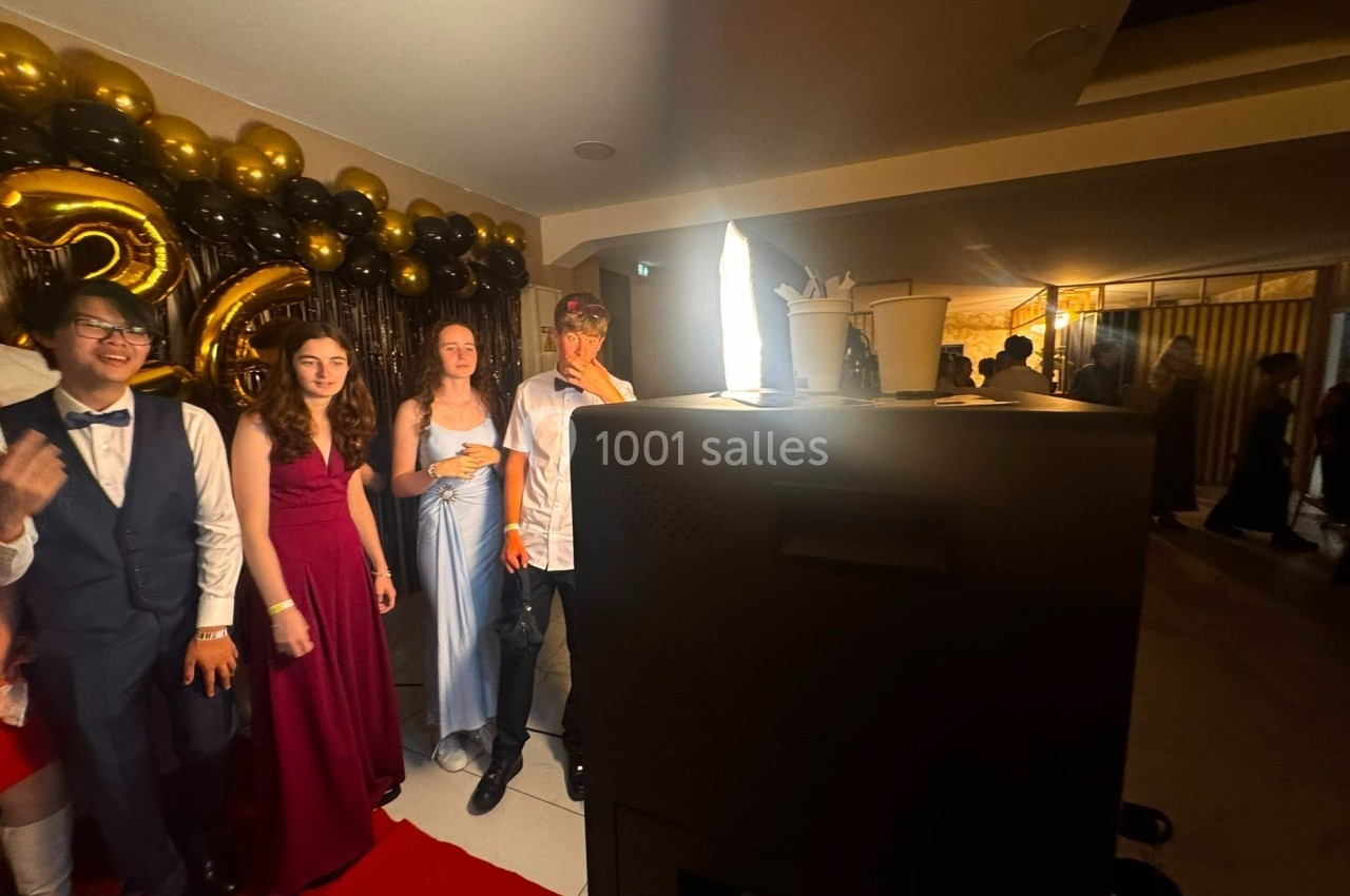 Des jeunes posent sur un tapis rouge devant un mur décoré de ballons noirs et dorés, éclairés par une lumière vive.