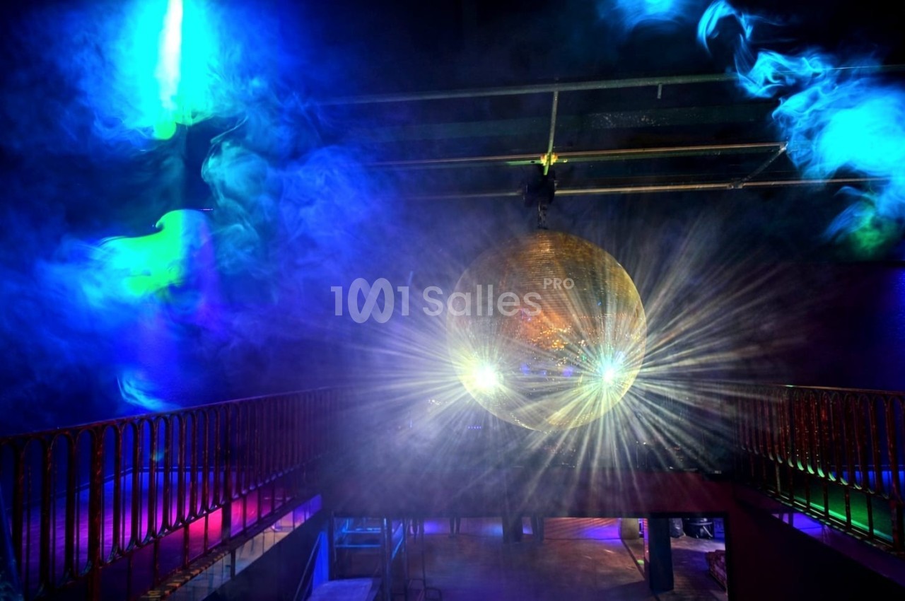 Une boule disco dorée suspendue reflète des faisceaux lumineux colorés dans une salle obscure avec de la fumée.
