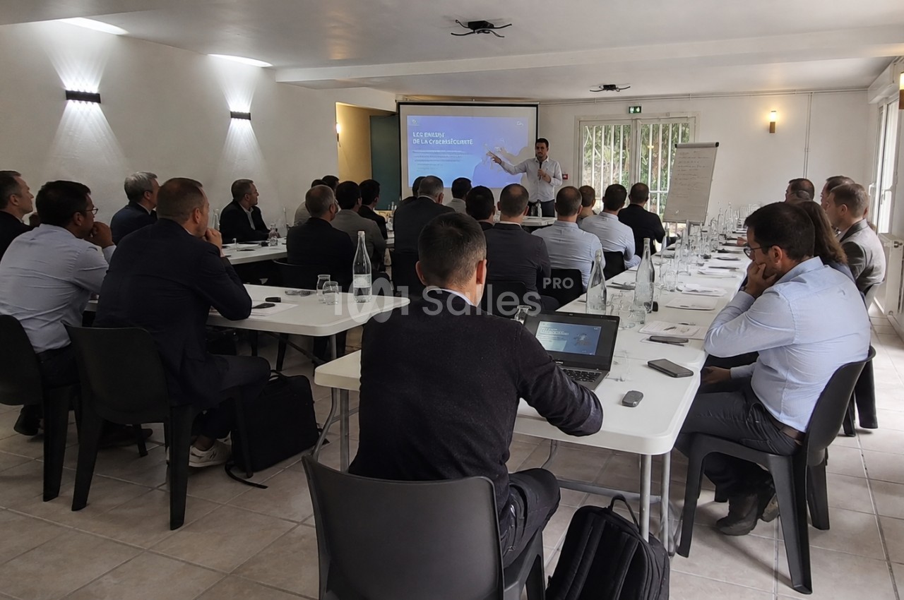 Un groupe de personnes assises dans une salle de réunion, écoutant une présentation projetée sur un écran.